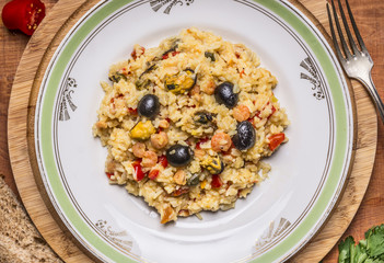 paella with seafood shrimp and mussels olives on a white plate on a cutting board on wooden background close up top view