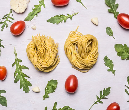 raw pasta cherry tomatoes arugula heads of garlic on a white rustic  wooden background top view