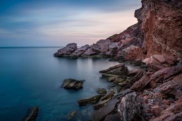 Fototapeta na wymiar Long exposure shot of Adriatic sea coast and red rock cliff. Sutomore, Montenegro