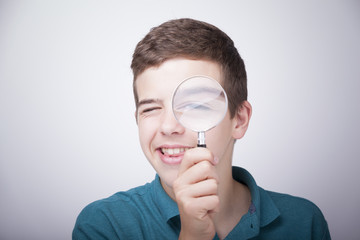 Boy looking through a magnifying glass against grey background