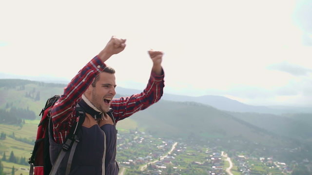 Ecstatic young hiker celebrating his achievement at the top of the mountain and looking down at a town below