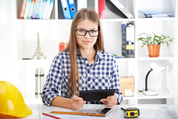 Cheerful woman with tablet pc sitting at the desk in engineer's office. Young woman studying CAD. 