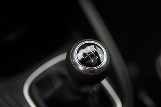 Close up of a manual shifter in a new car. The shifter is black and silver and made of leather.