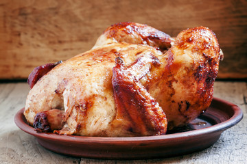 Whole roast chicken with a ruddy crust on a clay dish on the old