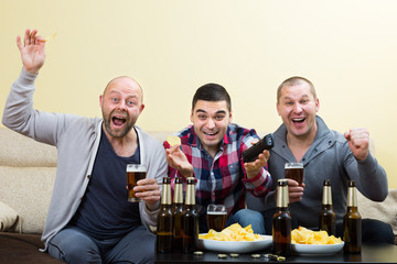 Three men watching football with beer indoor