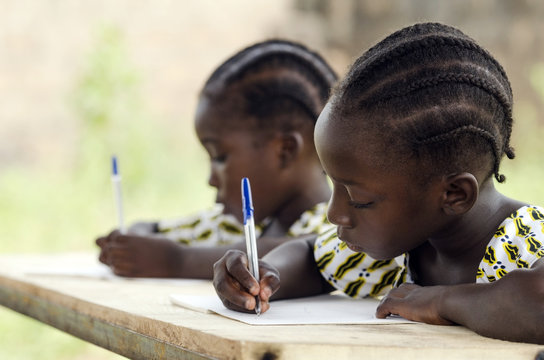 African Children at School Doing Homework. African ethnicity students writing their essay in an African school. They're holding blue pens to write down their homework whilst sitting in their desk. - Powered by Adobe
