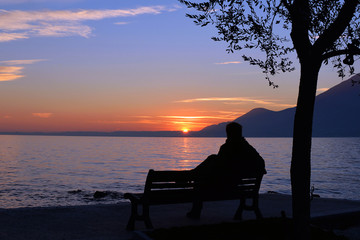 beautiful sunset on the lake with silhouette of a man meditating on a bench