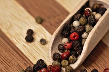 Grains of colored pepper on a wooden plank.