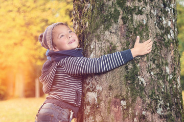 Lächelnder Bengel hält großen alten Baum fest