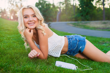 Happy young Caucasian blonde woman with tablet in park on sunny day on grass. Modern lifestyle and relaxation concepts