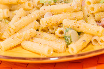 Pasta integrale con pesto al pistacchio, pancetta e zucchine, su tovaglietta arancione e piatto giallo