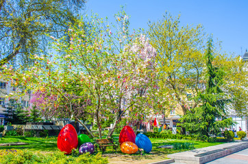 group of young people is sitting under a tree decorated by ribbons and easter eggs during easter time in bulgarian city plovdiv.
