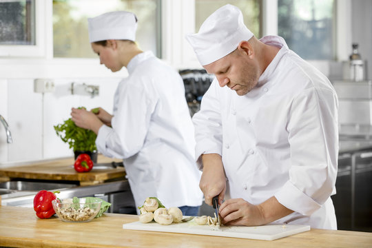 Two professional chefs preparing vegetables in large kitchen