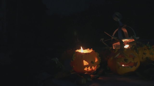 Side slide of Halloween pumpkins at night illuminated with candles, lateral slide shot
