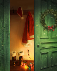 Open rustic door with Santa outfit hanging on hooks