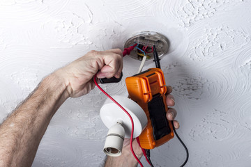 electrician testing a ceiling mounted light fitting