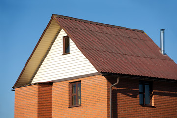 Fototapeta na wymiar New country house of red brick, brown roof covered and siding on the front and a metal chimney
