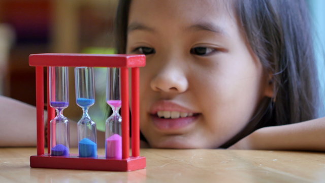 Little Asian child looking at hourglass in class