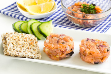 Salmon tartare with vegetables and crisp bread on a kitchen table.