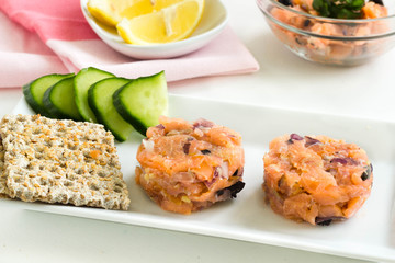 Salmon tartare with vegetables and crisp bread on a kitchen table with pink table cloth.