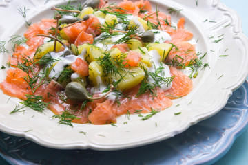 Dill-Kartoffelsalat mit Lachs und Kapernäpfeln auf weißem Teller mit blauem Platzteller