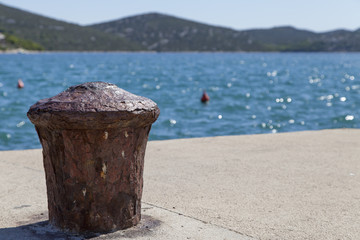 Naklejka premium Metal mooring bollard on the dock of concrete harbor pier, selective focus on bollard, space for text