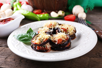 Dish of eggplant with cherry tomatoes and cheese in white plate on wooden table, closeup
