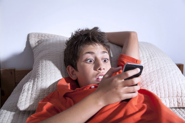 Surprised young boy is playing with smart phone