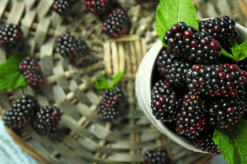 Heap of sweet blackberries with mint in cup on table close up