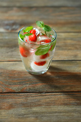 Glass of cold refreshing summer drink with berries and ice cubes on table close up