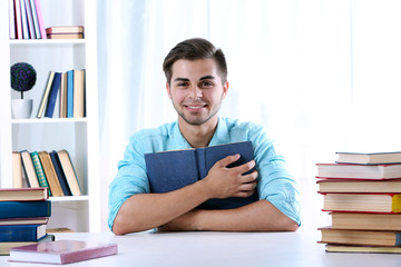 Young man reading book at table in room