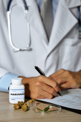 Doctor writing on prescription blank and bottle with medical cannabis on table close up