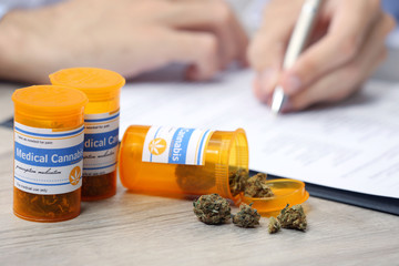 Doctor writing on prescription blank and bottle with medical cannabis on table close up