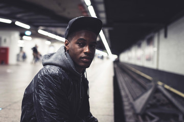 Urban fashion afro man sitting on ground of subway station.