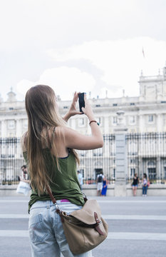 Beautiful young blond woman taking pictures of the Royal Palace in Madrid.