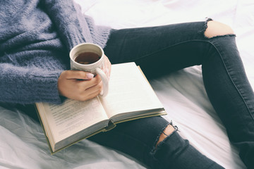 Obraz premium Woman on the bed with old book and cup of coffee, top view point