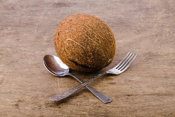 coconut on a wooden background, fork with spoon is crosswised in front of it