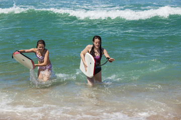 Girls Ocean beach walking out with body boards