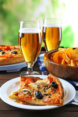 Sliced pizza served with beer on wooden table