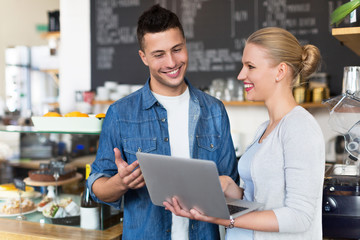 Young cafe owners looking at laptop