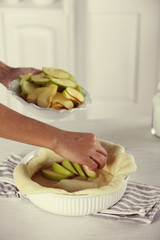 Woman making apple pie on wooden table, on light background