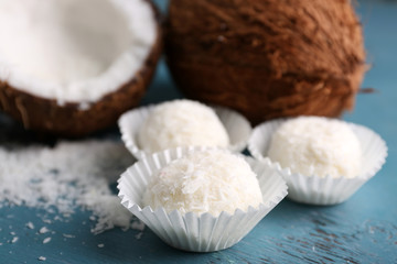 Candies in coconut flakes and fresh coconut on color wooden background