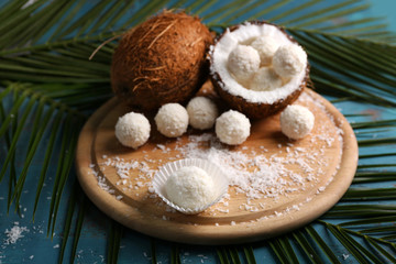 Candies in coconut flakes and fresh coconut on color wooden background