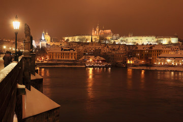 Night snowy Prague gothic Castle and St. Nicholas' Cathedral with Charles Bridge, Czech republic