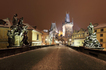 Obraz premium Night snowy Prague with Bridge Tower, St. Nicholas' Cathedral and gothic Castle from Charles Bridgel, Czech republic