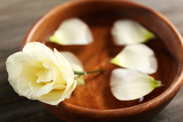 Flower petals in bowl with water on wooden background