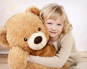 Little girl cuddling with her big plush teddy bear