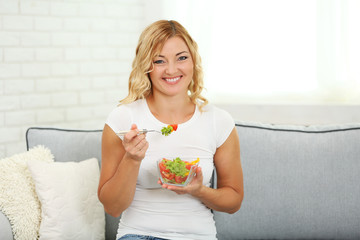 Beautiful woman with salad on home interior background