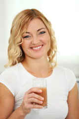 Beautiful woman with glass of juice on home interior background