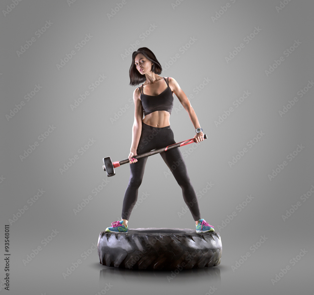 Wall mural Athletic young woman doing a fitness workout with hammer on gray studio background